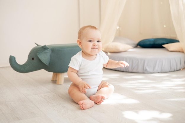 Niedlicher kleiner Junge in einem hellen Kinderzimmer mit einem Wigwam, der in einem Baumwollbody spielt und lächelt