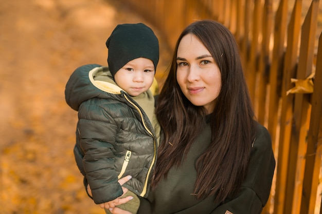 Niedlicher kleiner Junge steht mit seiner Mutter im Freien. Fröhliches Kind geht im Herbstpark spazieren. Kleinkind trägt trendige Jacke und Hut. Herbstmode. Stylisches Kind draußen