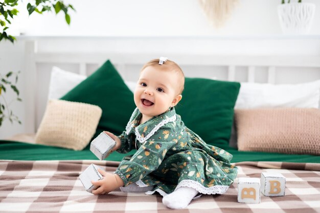 Niedliches kleines Mädchen in einem baumwollgrünen Kleid auf dem Bett im Wohnzimmer des Hauses, das lächelnd in die Kamera blickt