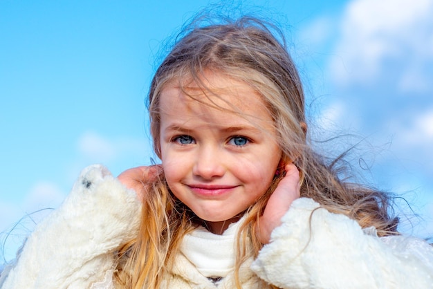 Niedliches kleines Mädchenporträt am blauen Himmel, lustige Kindergefühle im Freien, Nahaufnahmeporträt eines süßen Kleinen