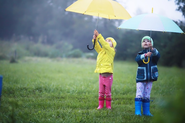 Niedliches Kleinkind, das an einem nebligen Herbsttag auf einer Landstraße im Regen mit Regenschirm spielt