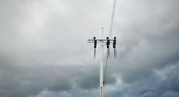 Niedrige Winkelsicht des elektrischen Pfostens und der Kabel gegen dunklen bewölkten stürmischen Himmel