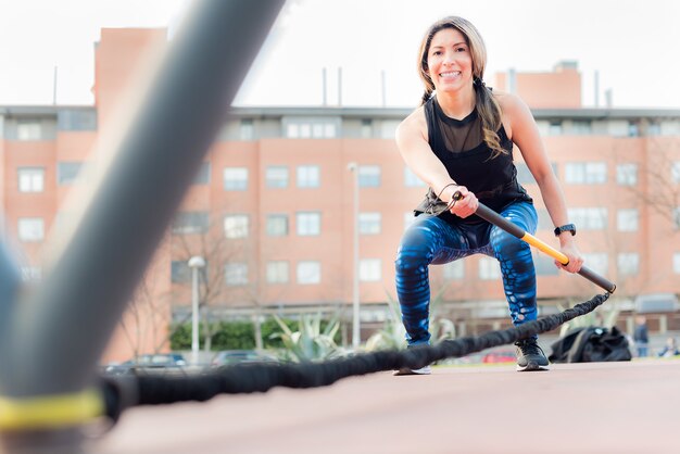 Niedrige Winkelsicht einer Fitnessfrau, die die Kamera anschaut, die mit einem elastischen Gymnastikstock im Park trainiert. Junge erwachsene Frau, die draußen trainiert.