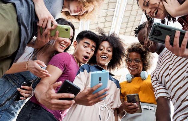 Foto niedrige winkelsicht einer gruppe junger teenager, die handys halten. überraschte gesichter schauen auf den bildschirm. konzept der technologie, verbindung, bunt.