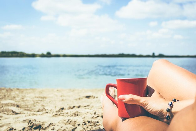 Foto niedriger abschnitt einer bikini-frau mit kaffeebecher, die sich am strand entspannt