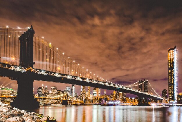 Foto niedriger blickwinkel auf die beleuchtete brücke über den fluss in der stadt bei nacht