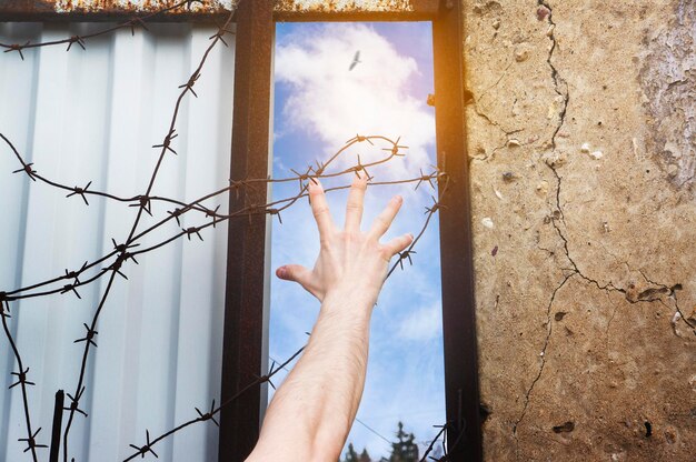 Foto niedriger blickwinkel der hand durch stacheldraht an der wand