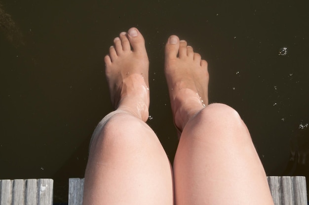 Foto niedriger teil einer frau, die auf dem pier über dem see sitzt