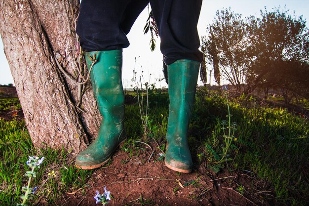 Foto niedriger teil einer person, die grüne gummistiefel trägt, während sie auf dem feld steht