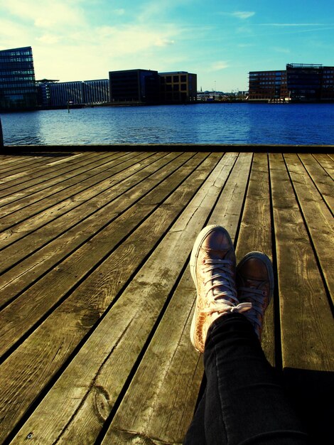 Foto niedriger teil einer person, die sich am pier vor dem fluss entspannt