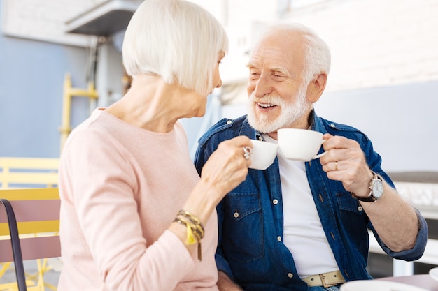 Niedriger Winkel des glücklichen älteren Paares, das am Café sitzt und Kaffee nippt