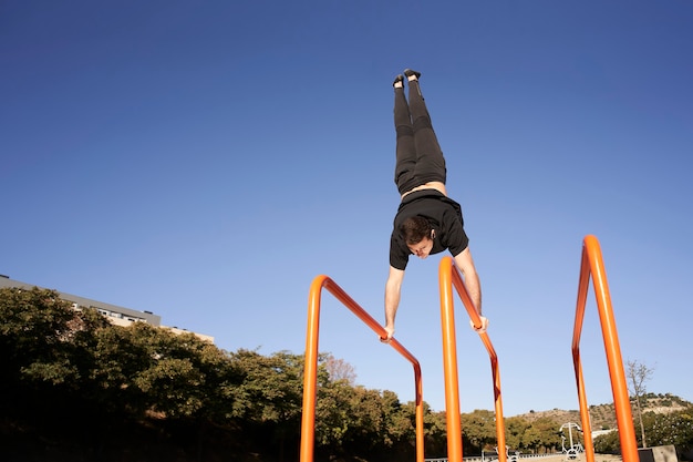 Niedriger Winkel eines Mannes, der Handstand auf der Stange tut. Bewegung im Freien. Konzept von gesundem Leben, Sport, Training, Krafttraining.