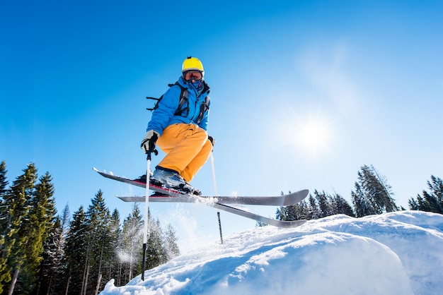 Niedriger Winkelschuss eines Skifahrers in der bunten Ausrüstung, die beim Skifahren auf einer Piste in die Luft springt