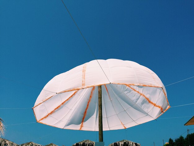 Niedrigwinkelansicht auf einen weißen Sonnenschirm vor einem klaren blauen Himmel