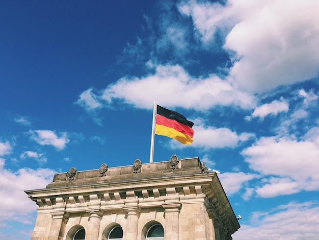 Niedrigwinkelansicht der deutschen Flagge auf dem Reichstag gegen wolkigen blauen Himmel an einem sonnigen Tag