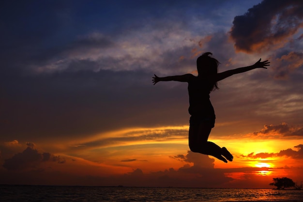 Niedrigwinkelansicht der Silhouette einer Frau, die gegen den orangefarbenen Himmel springt