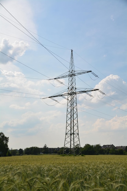 Niedrigwinkelansicht des Strompylons auf dem Feld gegen bewölkten Himmel an einem sonnigen Tag