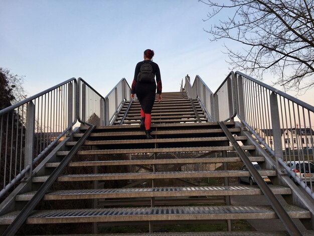 Foto niedrigwinkelansicht einer frau, die auf treppen gegen den klaren himmel in der stadt geht