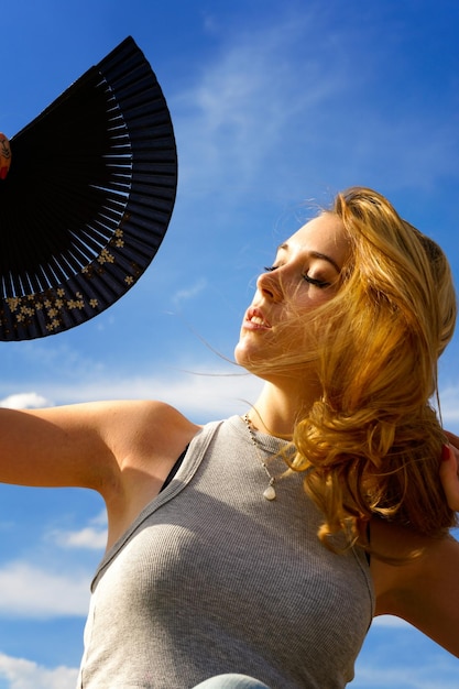 Niedrigwinkelansicht einer jungen Frau mit Handventilator gegen den Himmel an einem sonnigen Tag