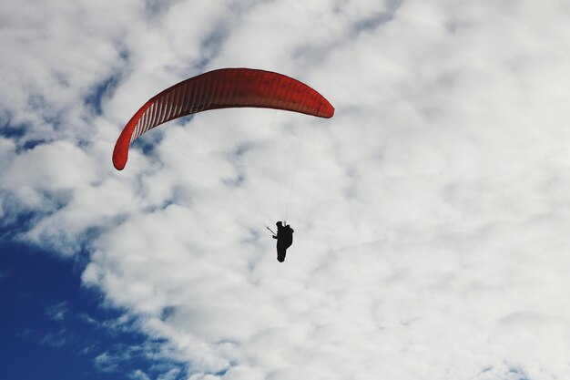 Foto niedrigwinkelansicht einer person, die gegen einen bewölkten himmel paragliding fährt