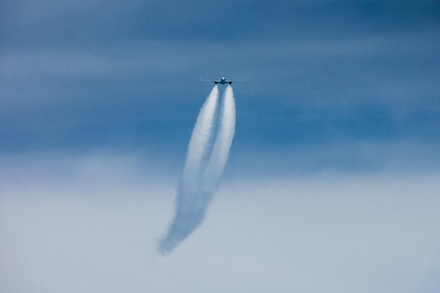 Foto niedrigwinkelansicht eines flugzeugs, das mit kondensstreifen im himmel fliegt