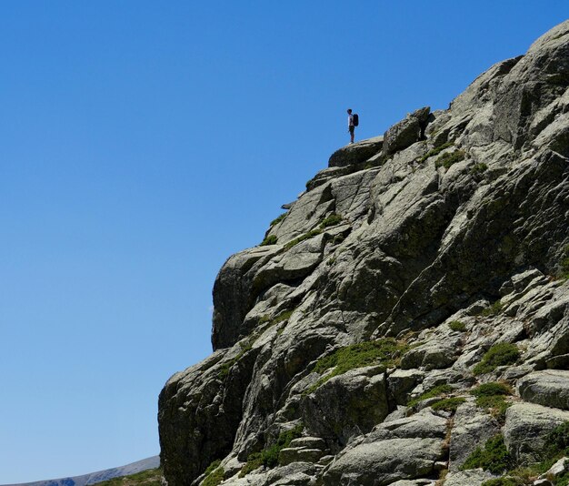 Foto niedrigwinkelansicht eines mannes, der am rand eines felsens gegen einen klaren blauen himmel steht