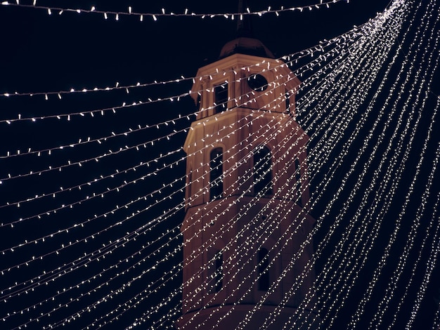 Niedrigwinkelansicht von beleuchteten Stringlichtern gegen die Kirche in der Nacht