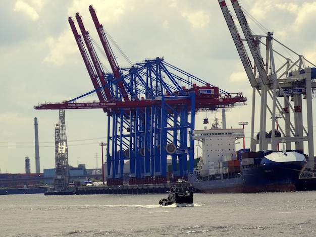 Niedrigwinkelansicht von Kränen am Fluss gegen den Himmel an einem sonnigen Tag im Hafen