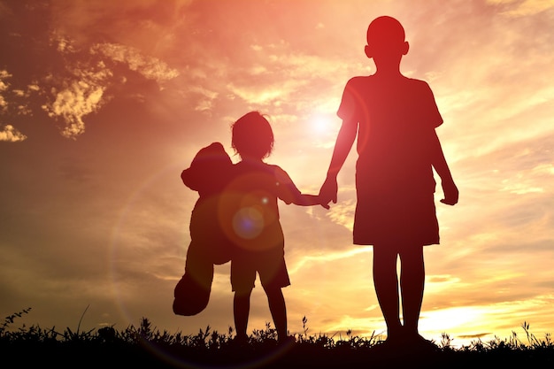 Niedrigwinkelansicht von Silhouetten von Kindern, die sich bei Sonnenuntergang am Himmel stehen und sich die Hände halten