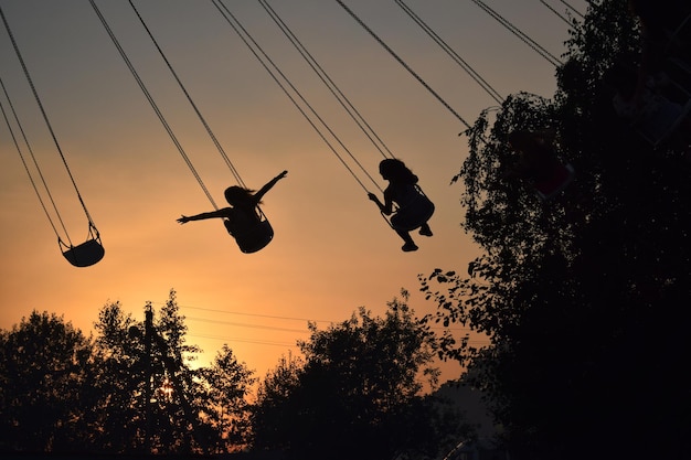 Niedrigwinkelansicht von Silhouetten von Menschen in einer Kettenschwungfahrt gegen den Himmel beim Sonnenuntergang