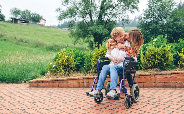 Foto la nieta abraza a la abuela en silla de ruedas en el parque