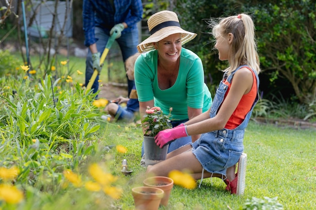 Nieta y abuela caucásicas sonrientes hablando en el jardín mientras trabajan en el jardín con su familia