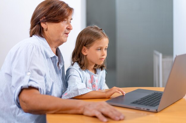 La nieta y la abuela enfocadas surfeando en la computadora portátil en casa