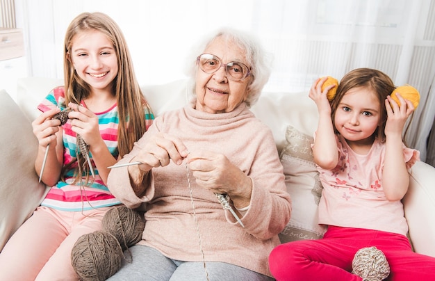 Nietas sonrientes con abuela tejiendo juntos