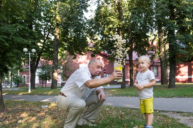 Un nietecito con pantalones cortos amarillos y un abuelo calvo lanzan alegremente palomitas de maíz al aire Un niño y un anciano se relajan en el parque
