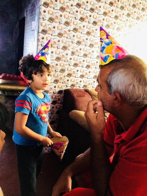 El nieto y el abuelo con sombreros de fiesta mientras están sentados en casa