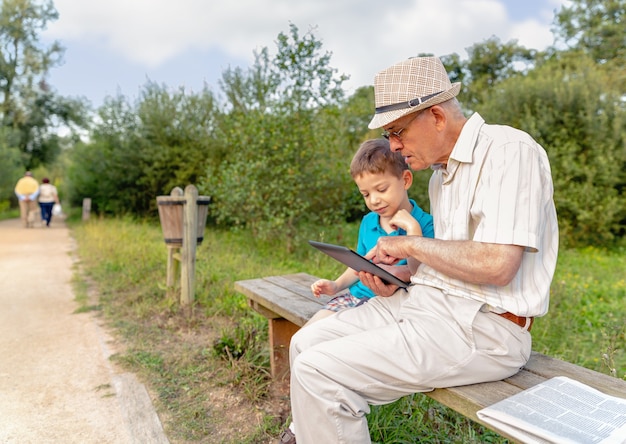 Nieto enseñando a su abuelo a usar una tableta electrónica en un banco del parque. Concepto de generación de valores.