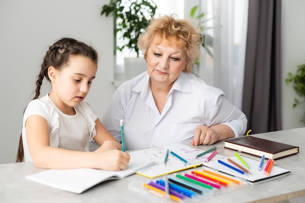 Nieto feliz con abuela divirtiéndose, dibujando lápices de colores, sentados juntos en casa, riéndose de una niña preescolar con una abuela sonriente pintando una foto, jugando con su nieta.