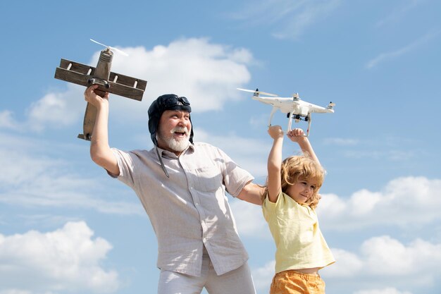 Nieto niño y abuelo sostienen avión y drone quad helicóptero contra cielo niño piloto aviador con...