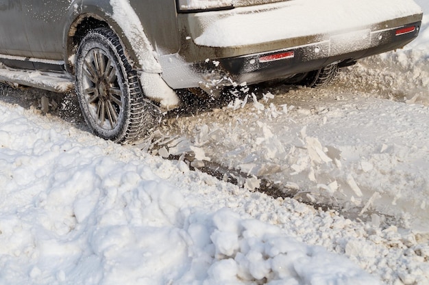 La nieve de la carretera sale volando de la rueda giratoria de un vehículo Las ruedas del coche giran y arrojan pedazos de nieve que intenta ganar tracción en la carretera resbaladiza