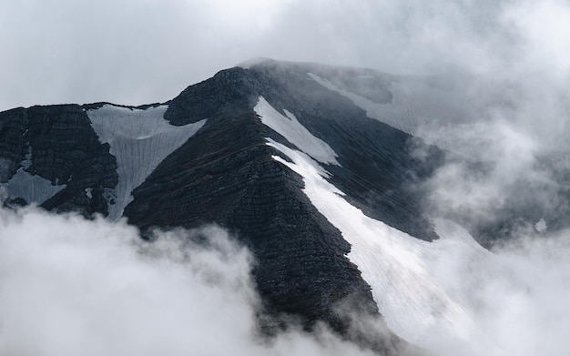 Nieve en la cima de la montaña, hermosas fotografías del cielo brumoso y montañas invernales. Vista exterior, acantilado rocoso. Turismo de invierno. Nubes alrededor de la montaña