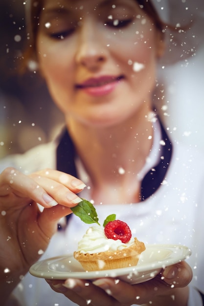 Foto nieve contra el jefe de cocina centrado que pone una hoja de menta en un pequeño pastel en un plato