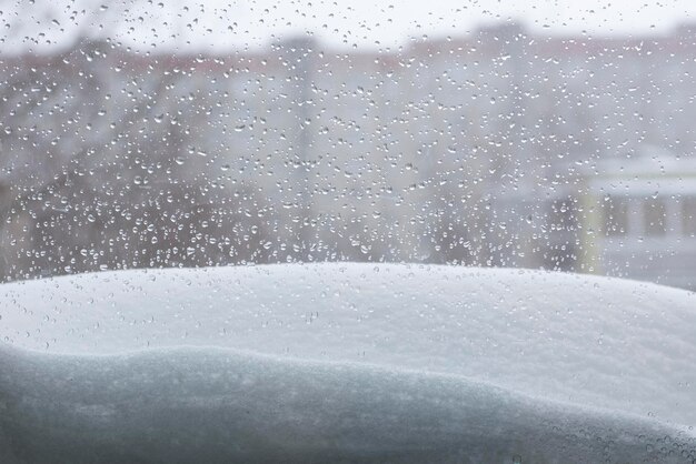 Nieve y gotas de lluvia detrás del cristal en una mañana de invierno