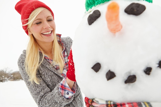 Nieve de invierno y mujer construyendo un muñeco de nieve al aire libre durante la Navidad en Inglaterra con felicidad Sonrisa temporada festiva y hombre de nieve de Navidad siendo construido por una mujer feliz al aire libre en clima frío