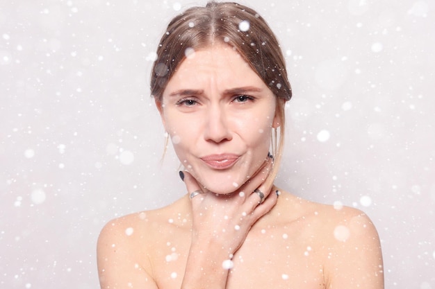 Nieve, invierno, navidad, enfermedad, salud, personas, concepto de medicina - dolor de garganta. Primer plano de una mujer enferma con dolor de garganta que se siente mal. Hermosa chica tocando el cuello con la mano sobre fondo de nieve