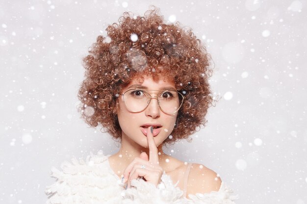 Nieve, invierno, Navidad, gente, concepto de belleza - Retrato de mujer negra joven sonriente. Retrato de una joven y bella mujer con corte de pelo afro afroamericano usando anteojos sobre fondo de nieve