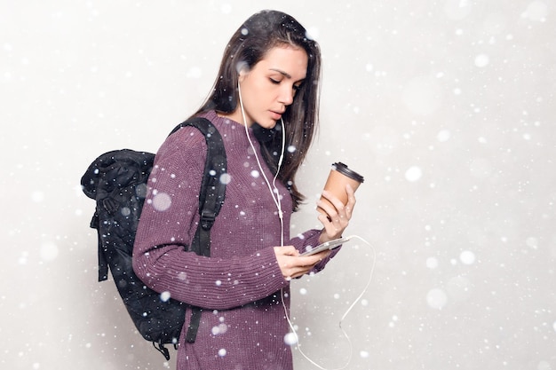 Nieve, invierno, navidad, tecnología, estilo de vida, adicción a internet y concepto de personas - mujer hermosa joven con teléfono inteligente. Sonriente mujer atractiva mirando el fondo de nieve del teléfono móvil