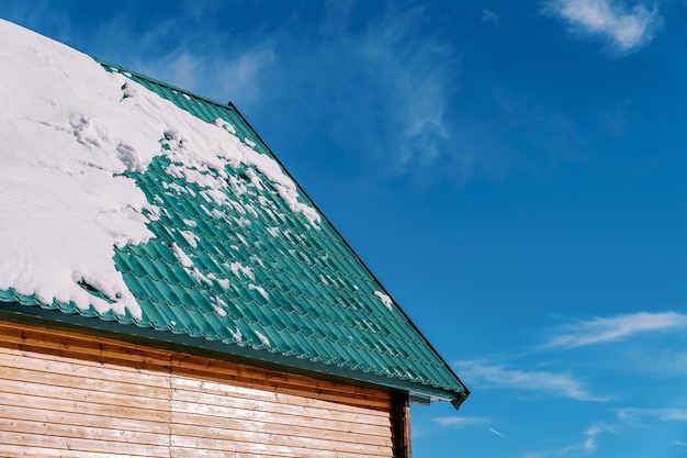 La nieve yace sobre el techo de tejas verdes de una cabaña de madera contra el cielo azul