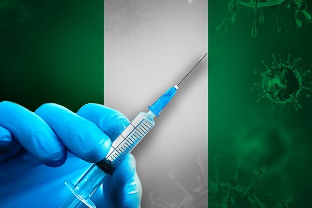 Nigeria Campaña de vacunación Covid19 Mano en un guante de goma azul sostiene una jeringa delante de la bandera