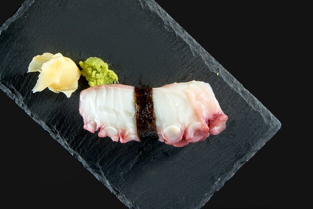 Nigiri-Sushi mit Tintenfisch auf einem schwarzen Brett mit Ingwer und Wasabi. Japanische Küche. Lebensmittellieferservice. Isoliert auf schwarz